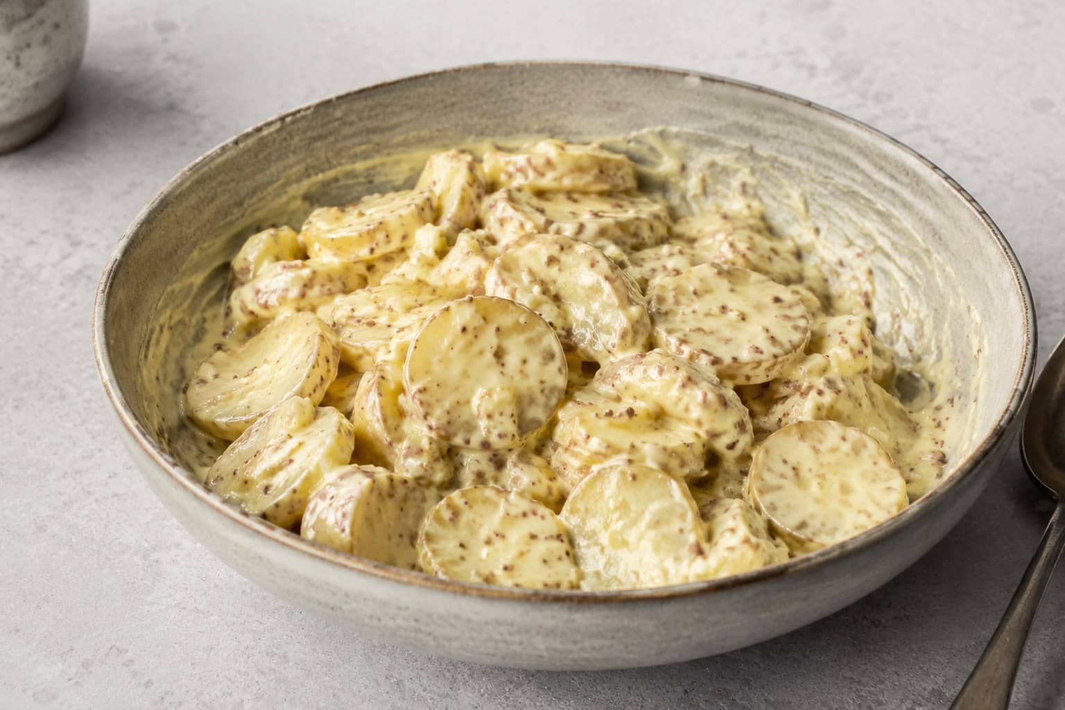 Skål med kartoffelsalat af halverede nye kartofler vendt i cremet sennepsdressing, toppet med purløg