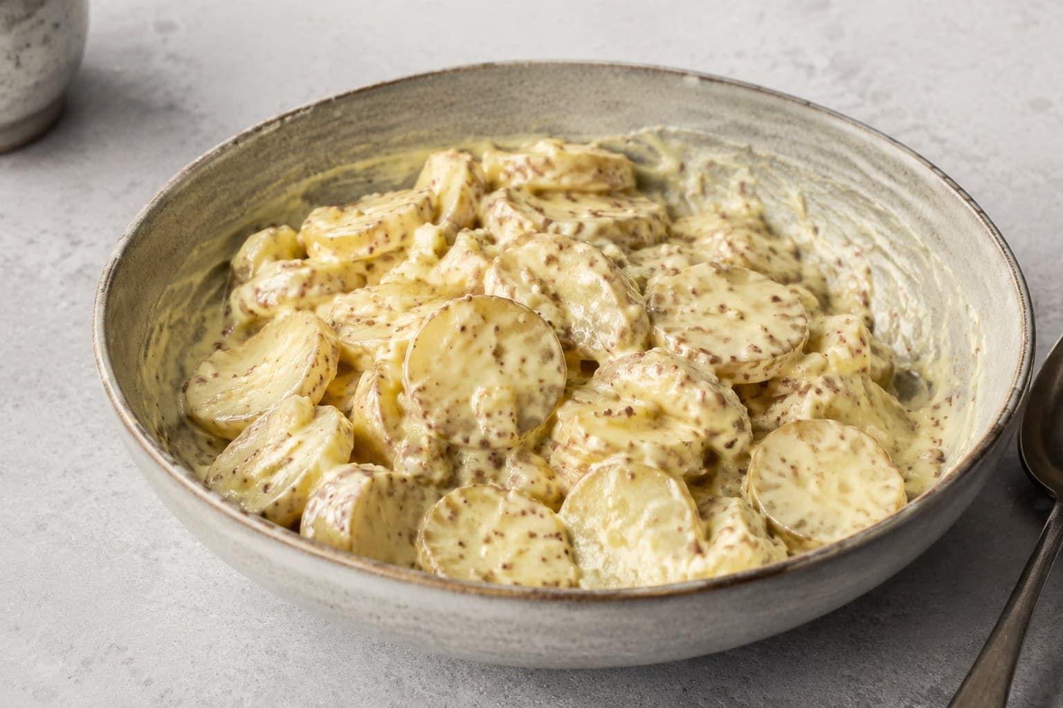 Skål med kartoffelsalat af halverede nye kartofler vendt i cremet sennepsdressing, toppet med purløg