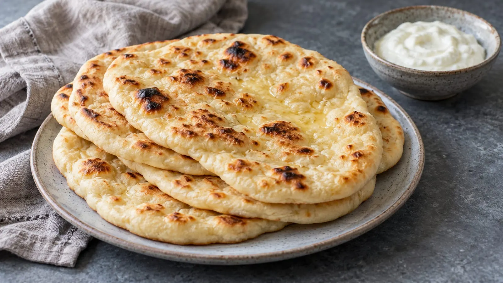 Stak af bløde naanbrød med hvidløgssmør og en skål yoghurt